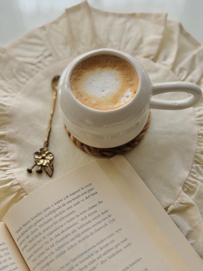 team-02 A warm latte on a textured cloth with an open book and floral spoon, ideal for relaxation.