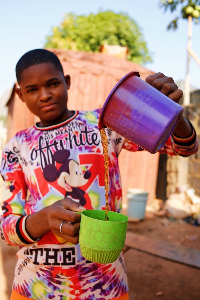 team-04 A young man in a vibrant shirt pouring tea from a purple cup outdoors in Abuja, Nigeria.