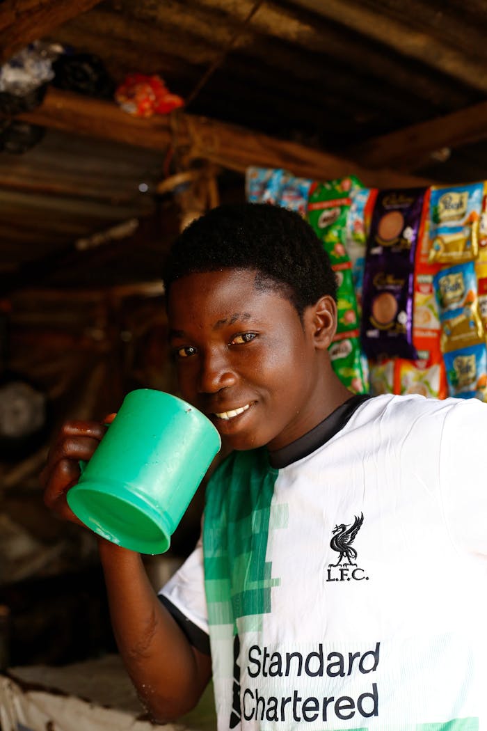 Smiling young man drinking from a green cup in a local Abuja shop.
