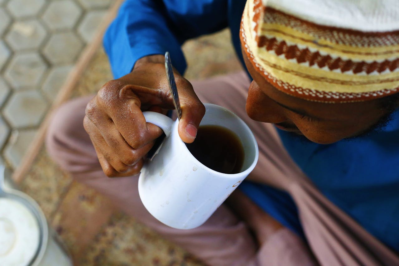 A man in traditional attire enjoys a cup of tea outdoors in Abuja, Nigeria.