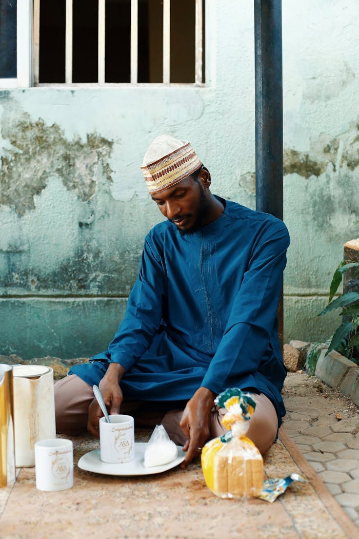 team-03 A man in traditional attire prepares breakfast outdoors, featuring bread and beverages.
